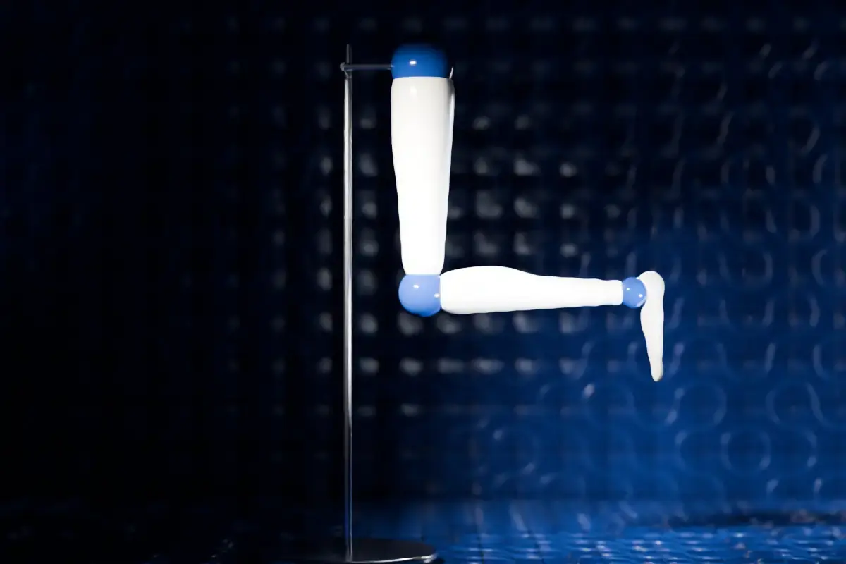 A white ceramic model leg on a steel stand, bent 90 degrees at the knee, in front of cobalt glazed tiles